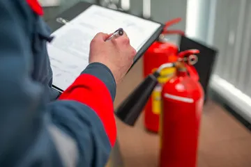 BSD Ulm Brandschutz Dienstleistungen -  Mitarbeiter notiert Prüfung neben roten Feuerlöschern